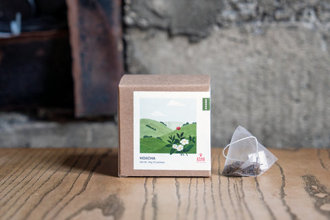 A labeled kraft box with a triangular tea bag (sachet), showcasing the product House Hojicha.